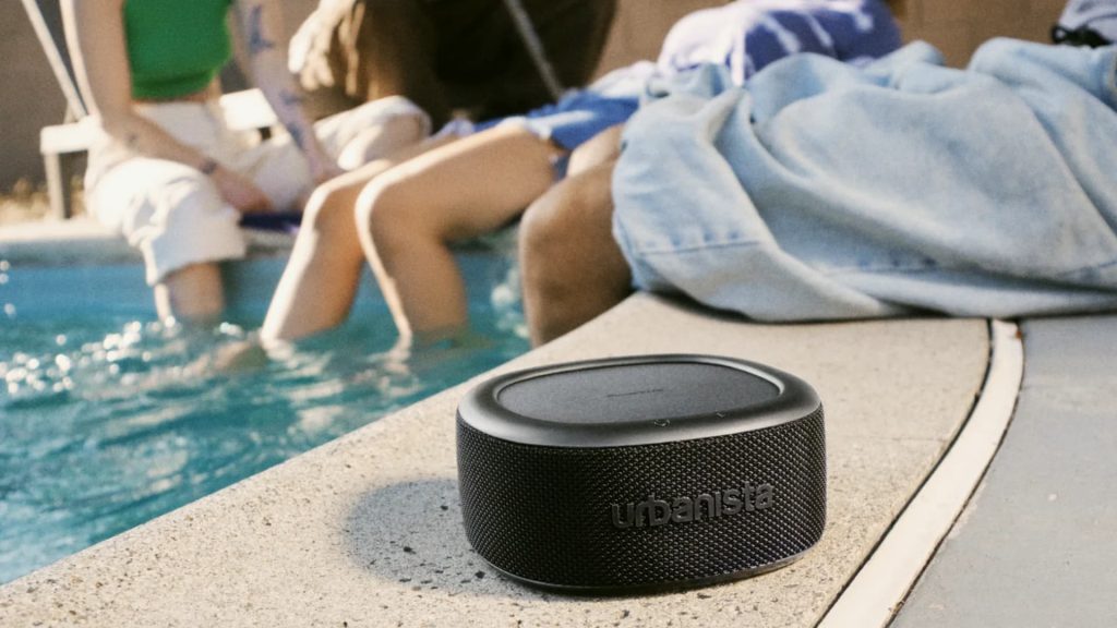 People chilling by the pool with an Urbanista Malibu portable speaker in black colour