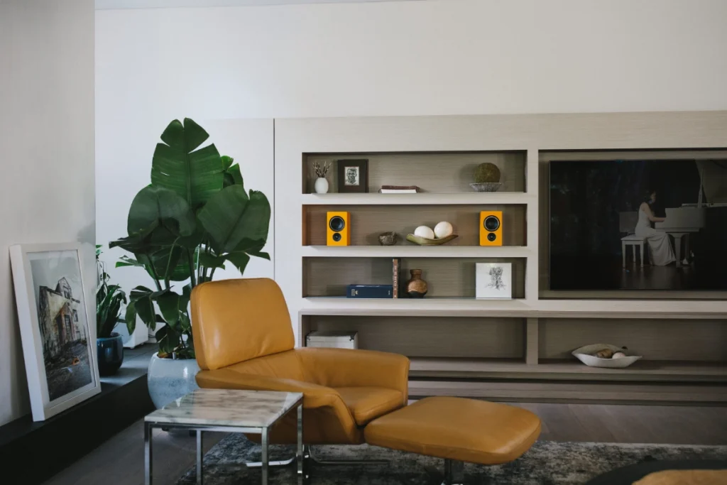 A stylish living room showcasing a yellow chair, a television, and yellow PSB Alpha iQ Speakers on a bookshelf.