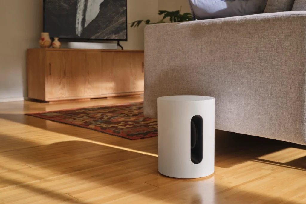 Sonos Immersive Set Beam set up in a cozy living room. Sub mini rests on the floor beside the couch, while the beam soundbar rests below the tv on top of a credenza