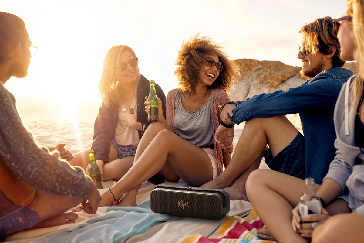 A group of friends enjoying the beach with a Klipsch Detroit Portable Speaker playing music nearby.