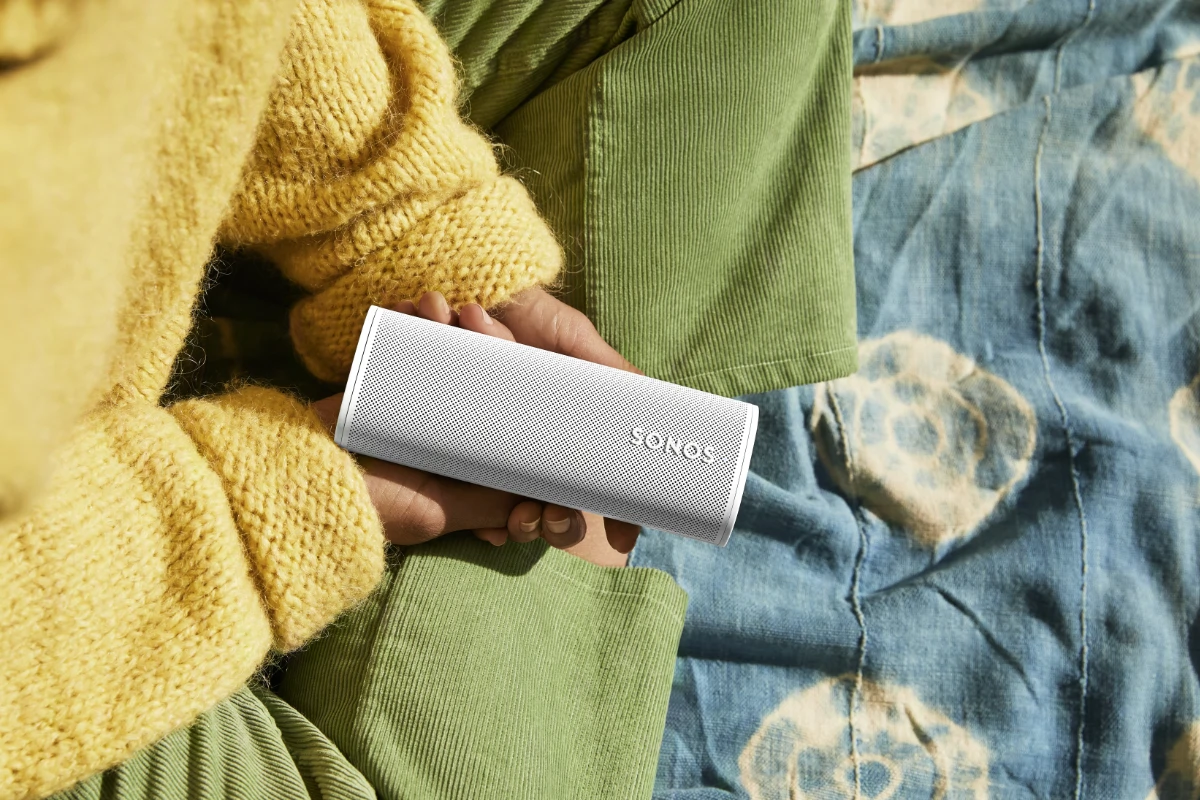 A person holding a white Sonos Roam 2 portable speaker in their hand, showcasing its compact and stylish design.
