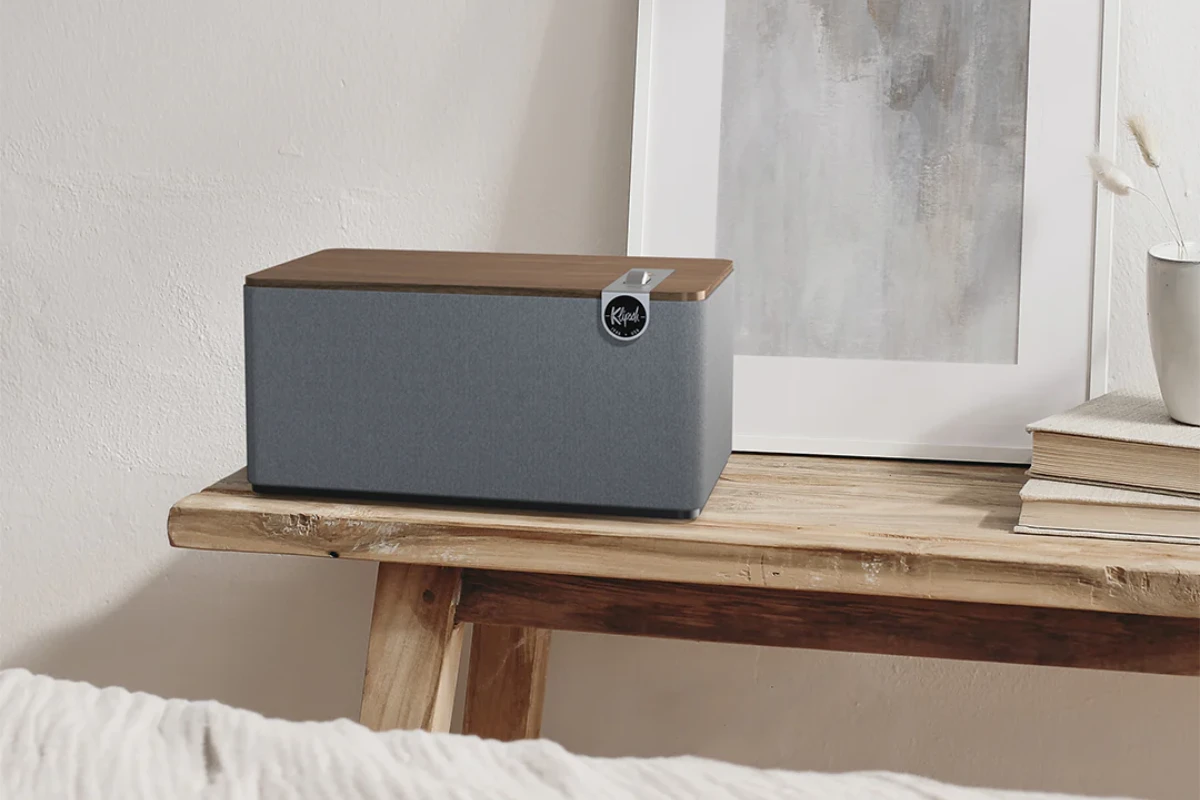 The Klipsch The One Plus speaker is placed on a wooden table, showcasing its compact design and elegant finish.