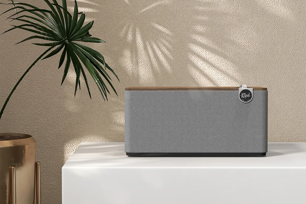 Klipsch Three Plus Walnut speaker resting on a white tabletop, next to a bright green plant