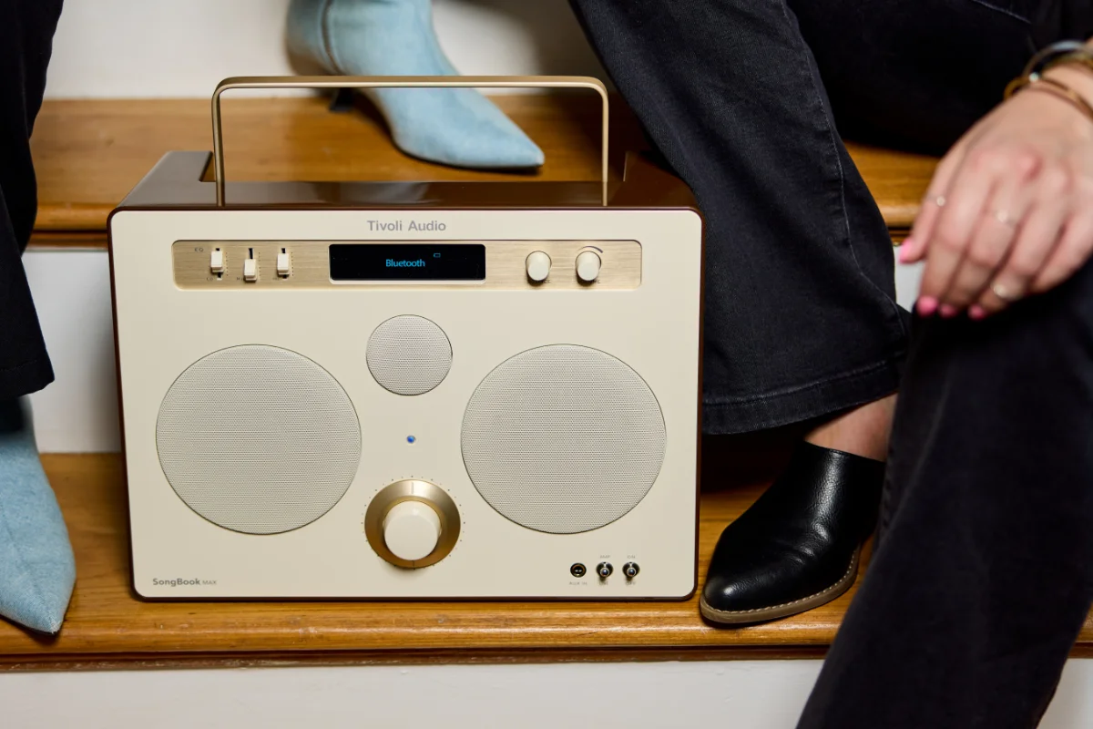 A woman in blue shoes stands beside a man in black shoes, surrounding a cream tivoli songbook max speaker