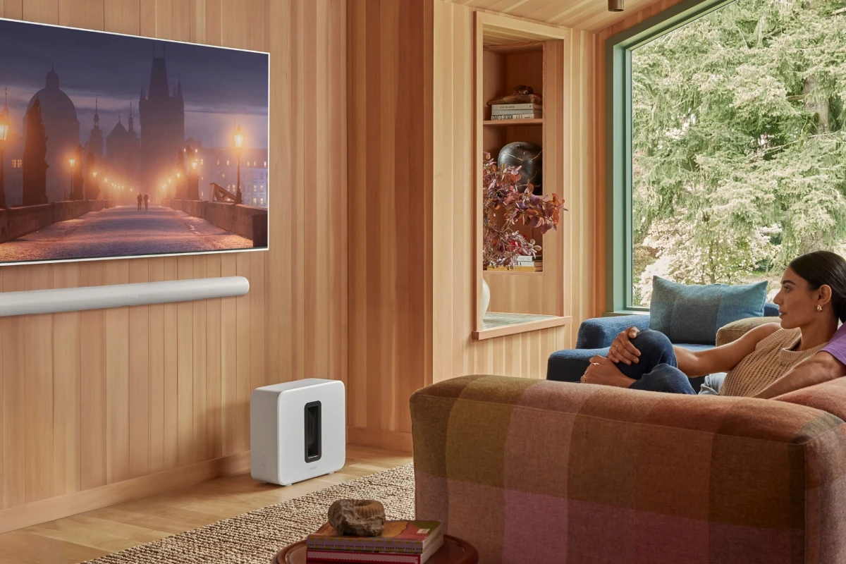 A woman watches tv on her couch while sound is played through a wall mounted sonos arc ultra in white