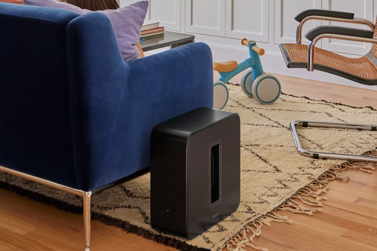 Sonos Sub 4 in matte black resting beside a couch in a cozy living room with childrens toys sprawled across the floor