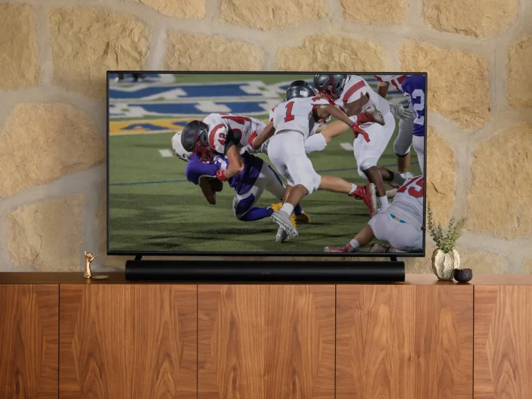 A TV broadcasting football in a quaint living room with a Sonos Arc soundbar in black beneath it.