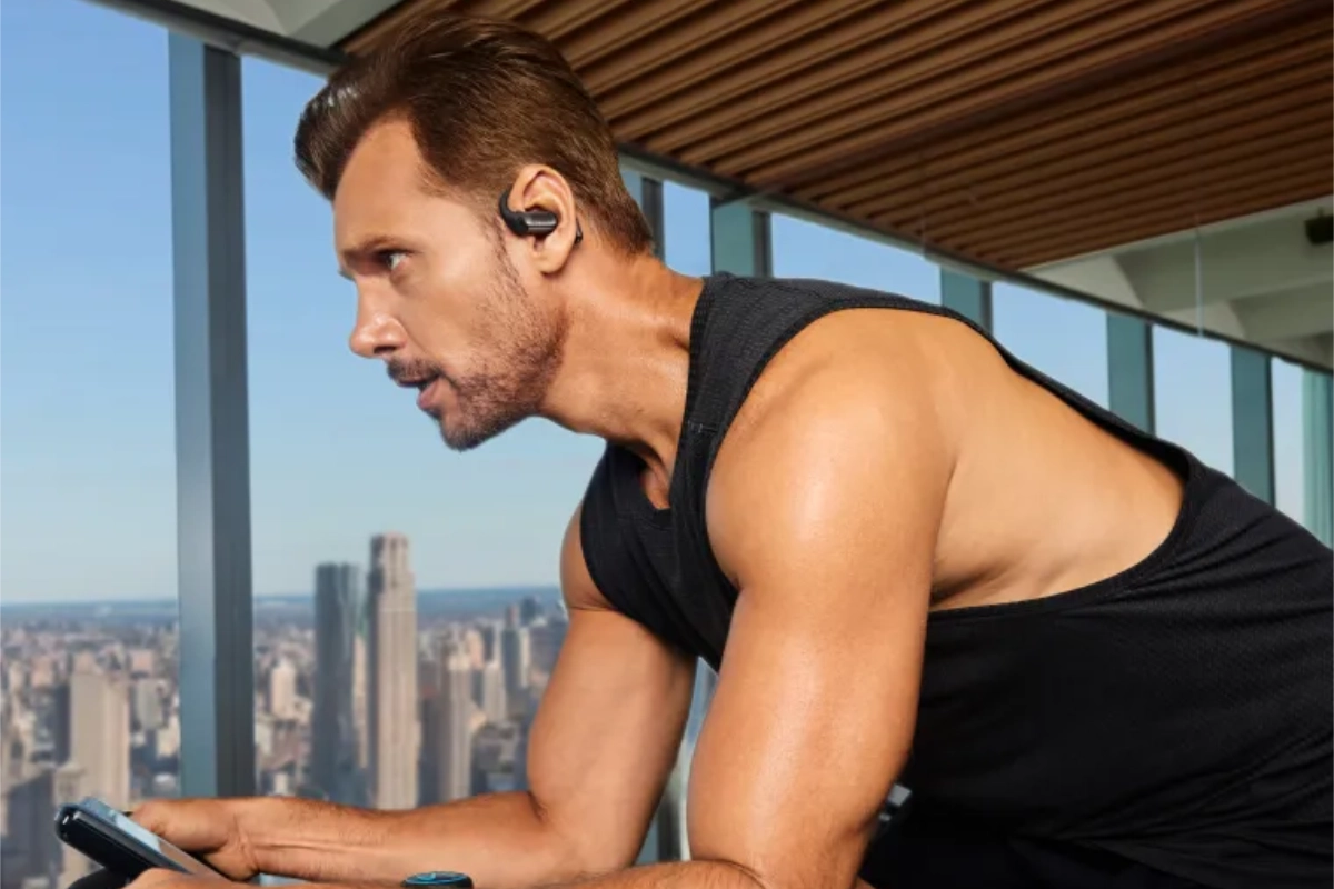 Man wearing a Shokz OpenFit Pro earbud while working out on an exercise bike.