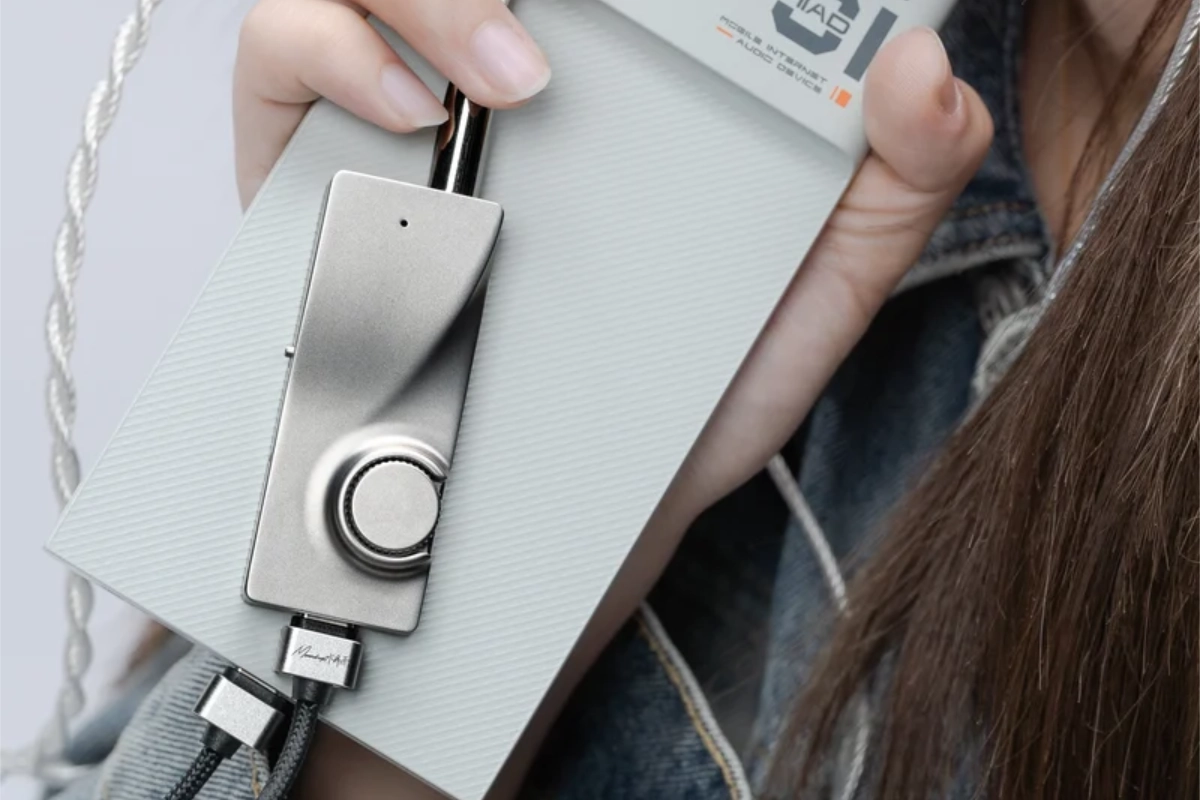 Person holding a phone with the Moondrop MoonRiver 3 DAC/amp attached via USB-C, showing its compact stainless steel design.